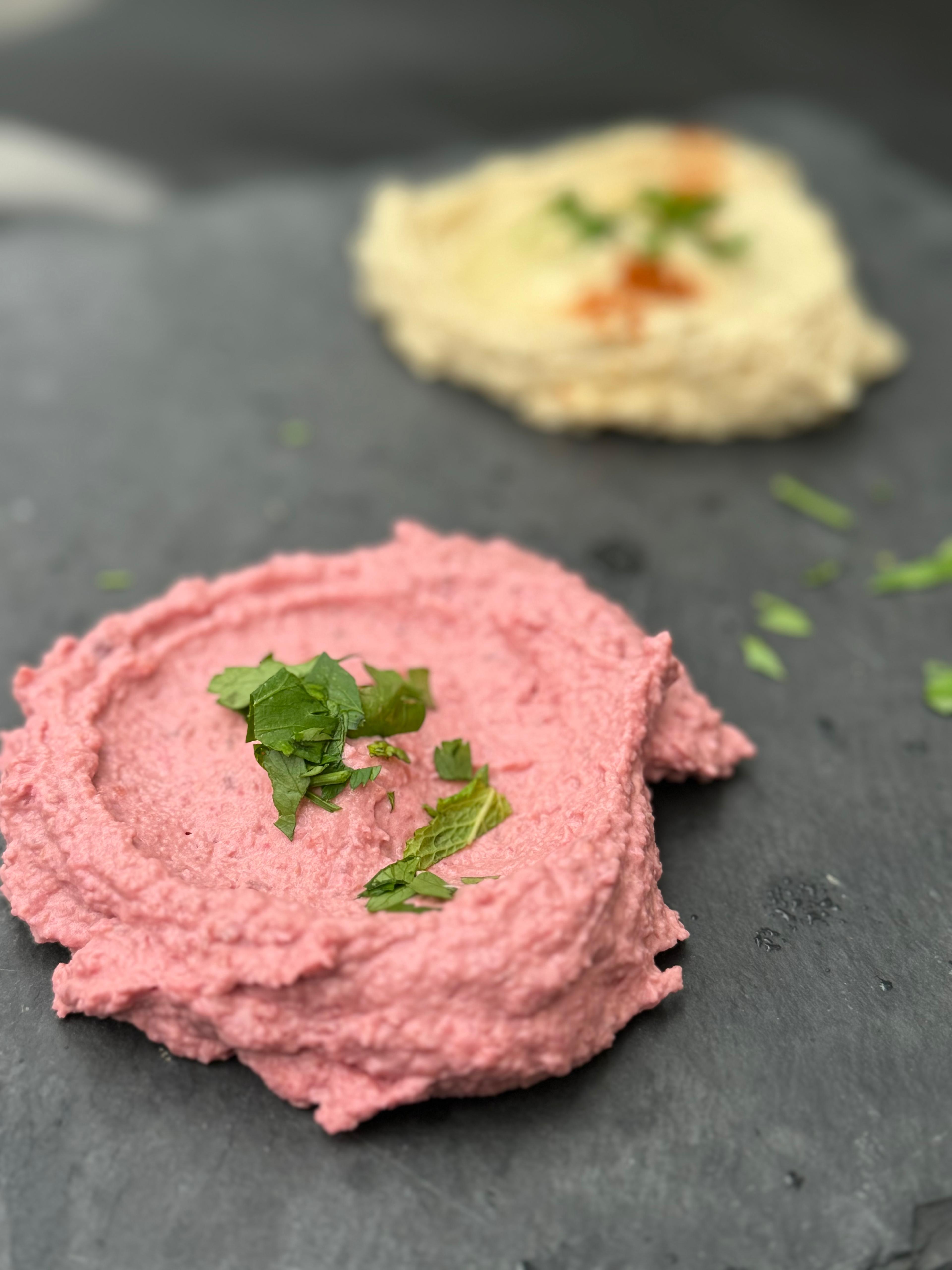 photo montrant du houmous de betterave en arrière plan, une entrée à base de pois chiches et de betterave, au premier plan, on voit du houmous.